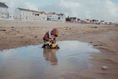 petit garçon joue camion plastique flaque de mer plage